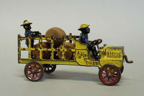 KENTON AUTO DRAY: C. 1911, cast iron, painted in yellow overall, open bench seat with stake side bed, red spoke wheels, embossed ''Auto Dray'' on cab sides, original standing figure in bed. 9'' long.