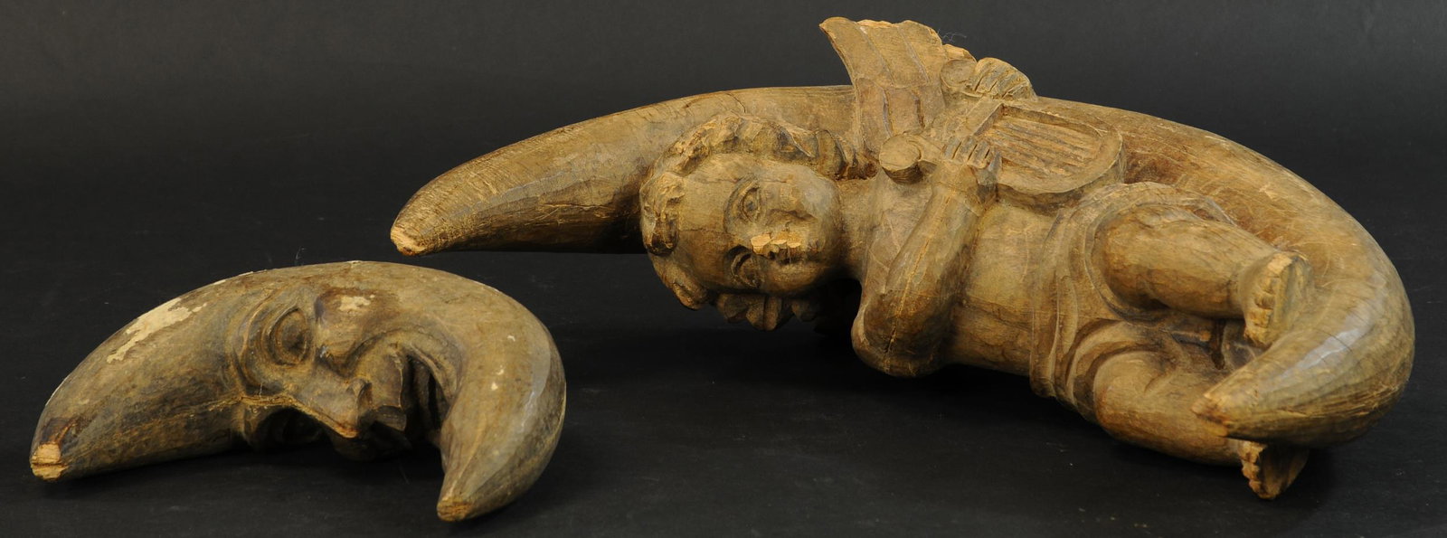 19TH CENTURY WOODEN CARVED CHERUB AND MOON: 215. 19TH CENTURY WOODEN CARVED CHERUB AND MOON | From Italy, a smiling man-in-moon and cherub with a harp on a quarter moon. 15" cherub, 7" man-in-moon | Some damage to nose of cherub and to tips of 