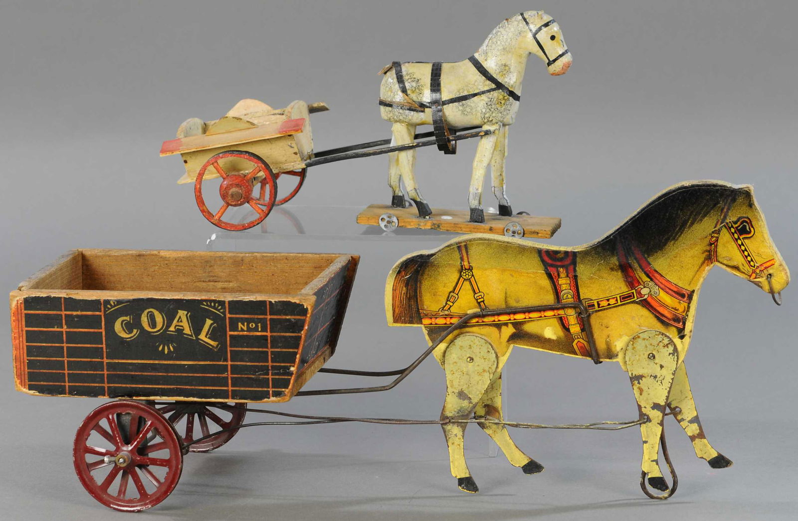 TWO HORSE & CART TOYS: 257. TWO HORSE & CART TOYS | A dapple grey w/wood cart and an articulated wood w/metal legs pulling a coal cart. Provenance: The Karyl Newman Christmas Collection. 11" to 19" | (Good Cond.) | $100 - $