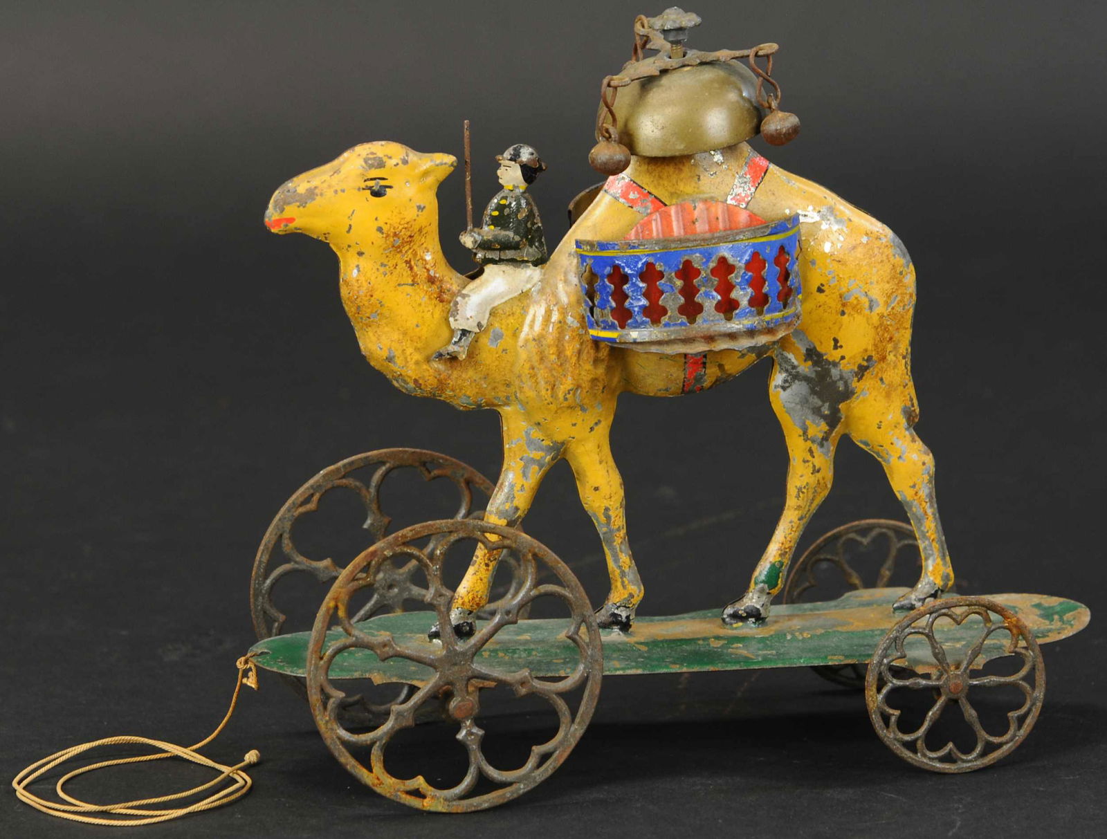 ALTHOF BERGMANN CAMEL BELL TOY: 44. ALTHOF BERGMANN CAMEL BELL TOY | Colorful hand painted tin, depicts man riding on camel with triple bell ringer on hump, heart shaped wheels at front are off-centered to cause an up and down motio