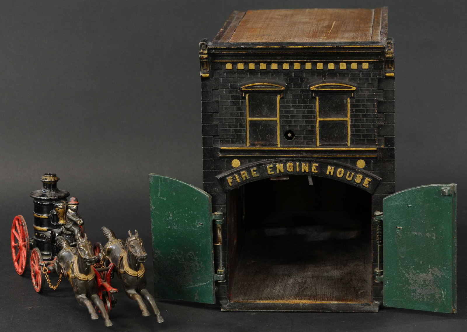 IVES CLOCKWORK FIRE HOUSE W/ PUMPER: 132. IVES CLOCKWORK FIRE HOUSE W/ PUMPER | Late 1890's, magnificent molding effect to the cast iron building facade, wood sides have cast iron window frames clockwork mechanism able to release the cas