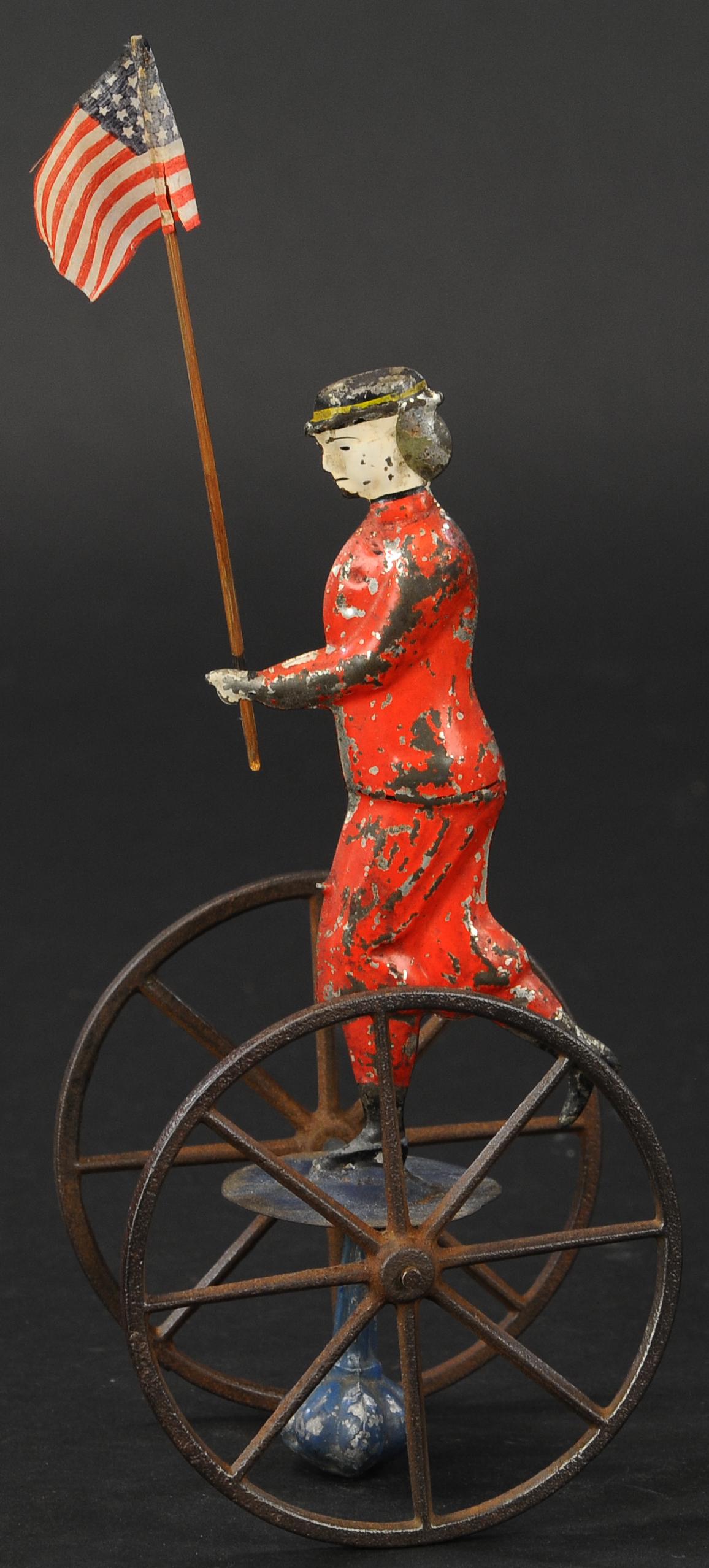 ALTHOF BERGMANN PATRIOTIC BALANCE TOY: 299. ALTHOF BERGMANN PATRIOTIC BALANCE TOY | Familiar suffragette style figure holding American flag appears on top of a two wheeled platform, large weight at bottom maintains her upright posture as t