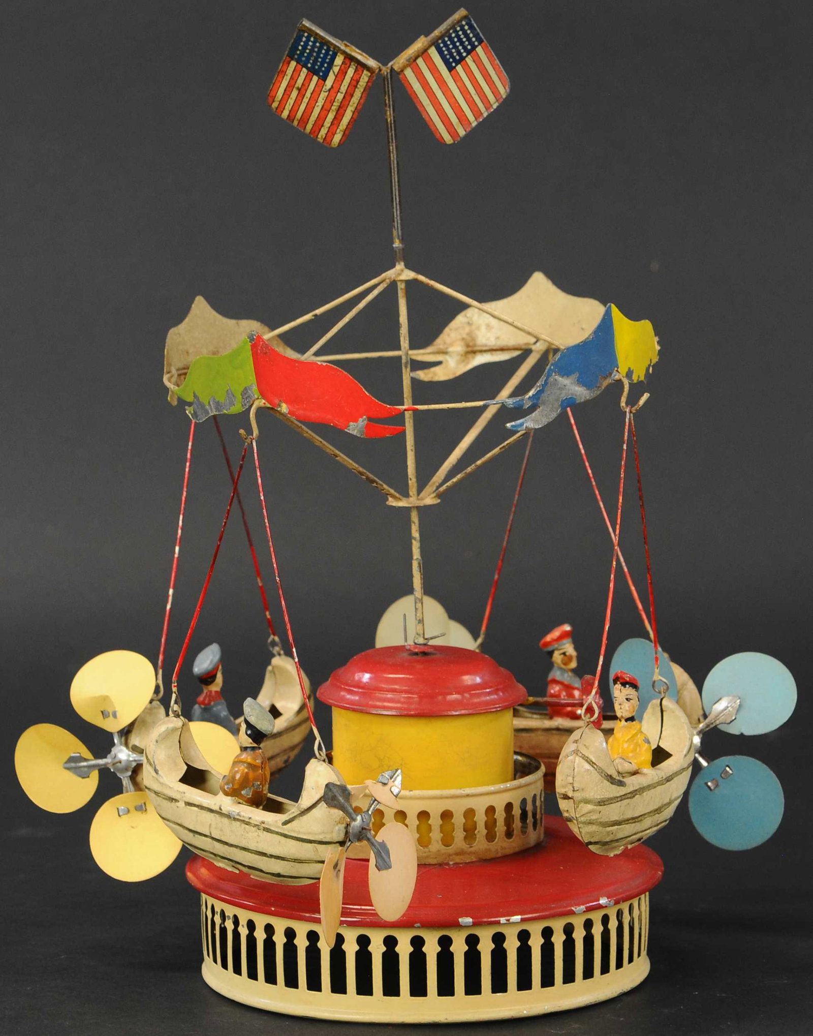 M&K GO AROUND W/ FLYING CANOES: 363. M&K GO AROUND W/ FLYING CANOES | Muller & Kadeder, Germany, c. 1909, tall example has dual tiered central base, clockwork driven and hand painted, features four gondola canoes with seated riders.