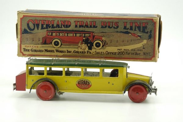 BOXED GIRARD "OVERLAND TRAIL" BUS: Lithographed tin, colorful example, done in yellow, green, red and black, keywind mechanism, seated driver, roof rack and rear simulated luggage compartment, decals on sides. 14" l.