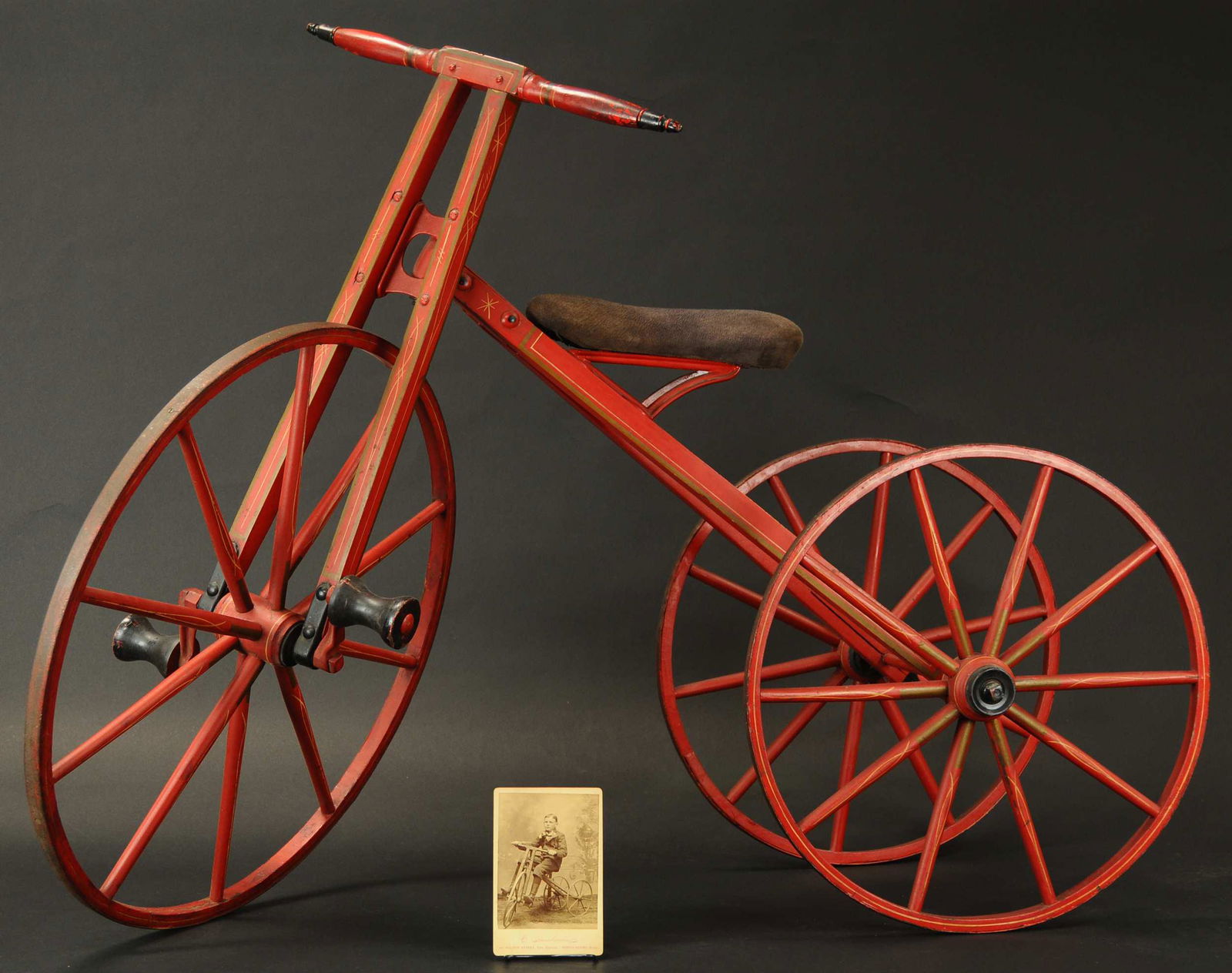 PAINTED WOOD BONE SHAKER TRICYCLE: 105. PAINTED WOOD BONE SHAKER TRICYCLE | All original early trike is made of wood, nicely hand painted in red with yellow striping, circa 1860-1880, includes black and white cabinet card photograph of