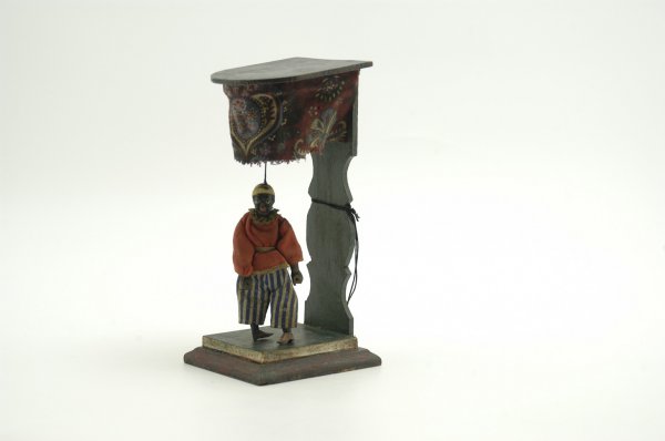 CAKE WALKER DANCING FIGURE: J. M. Cromwell, c. 1879, wooden stage platform, contains hanging figure able to tap on stage, fully dressed and hand painted. 9 3/4" h.