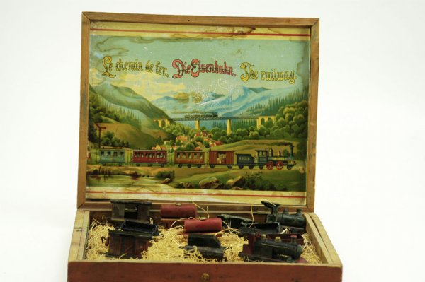 BOXED PENNY TOY RAILWAY SET: Germany, tin and lead train, locos, and cars; interior paper litho sheet depicts railroad crossing landscape, includes thirteen pieces. 9" x 11".
