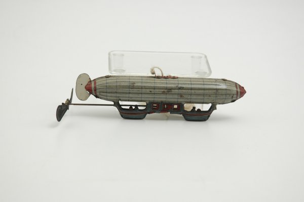 DIRIGIBLE PENNY TOY: Attributed to Distler, grey lithographed tin air ship has blue gondolas at belly and large green propeller. 6 1/4" l.