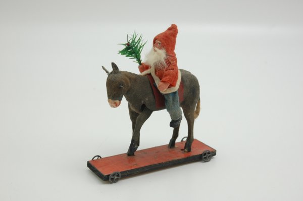 SANTA ON DONKEY PLATFORM TOY: Stamped Germany on bottom, red and black wheeled platform base holds composition faced Santa riding grey felt covered donkey who's left front leg raises when tail is lifted, Santa wears felt outfit an