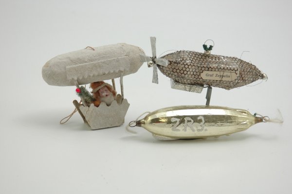 AIRSHIP ORNAMENTS AND CANDY CONTAINER: Group consists of a glass "Los Angeles" zeppelin, a Sebnitz style Graf Zeppelin with foil gondola and propeller, and composition faced Santa in mica covered airship with candy container gondola, made 