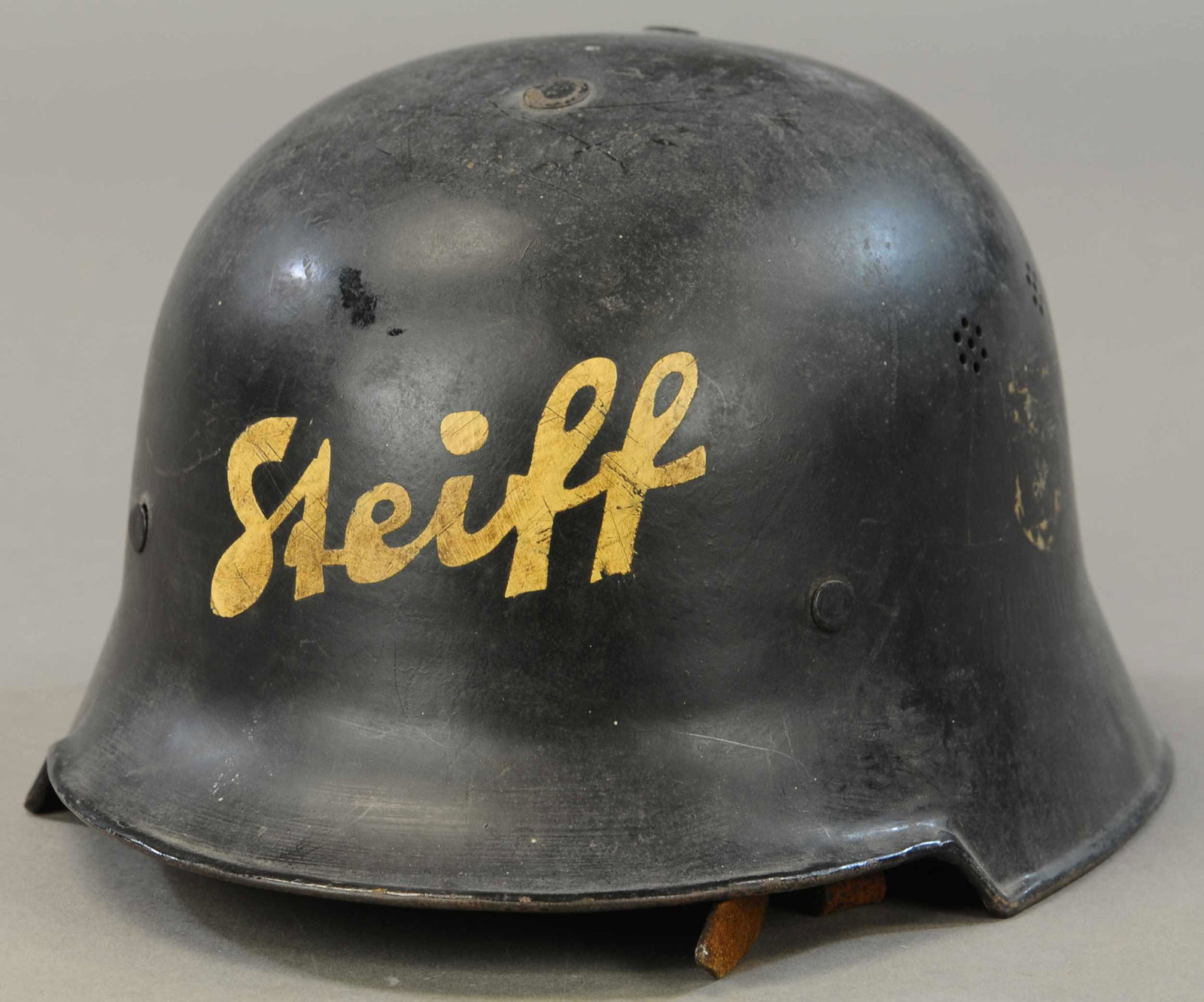 UNUSUAL METAL STEIFF SAFETY HELMET: 1234. UNUSUAL METAL STEIFF SAFETY HELMET | Black painted helmet with white "Steiff" signature, worn logos on each outer side, somewhat similar structure of a German military helmet, leather cushing an