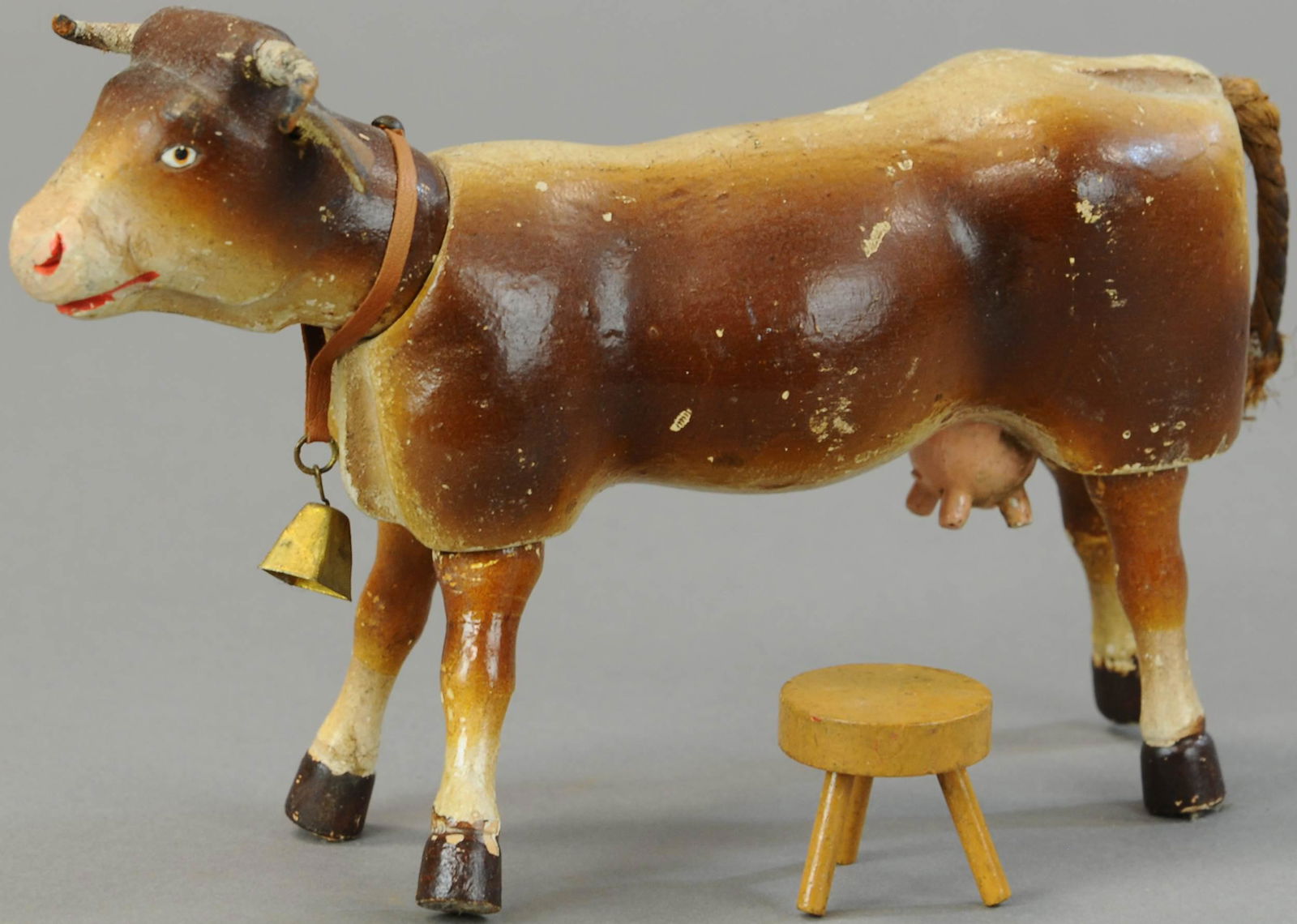SCHOENHUT COW WITH MILKING STOOL: 1289. SCHOENHUT COW WITH MILKING STOOL | Painted jointed wood, leather horns & ears, collar w/ brass bell. | 9" l. | (Exc. Cond.) | $250 - $500
