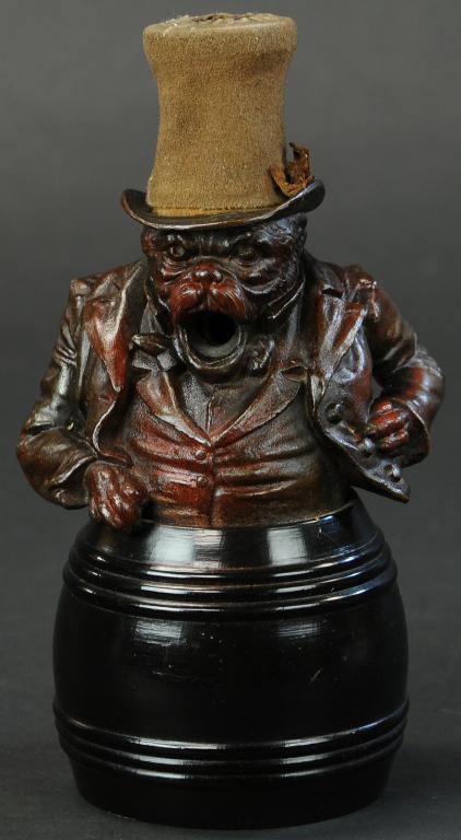 SUITED DOG IN BARREL CIGAR CUTTER: 908. SUITED DOG IN BARREL CIGAR CUTTER | Spelter figure, sitting on wooden barrel, also has a wooden plug in back of barrel for cutting; when the cigar is inserted in the figure's mouth, press the hat