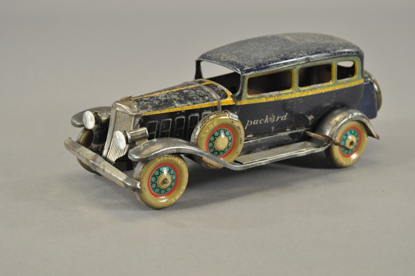 1933 PACKARD FOUR-DOOR SEDAN: Japan, Kosuge, lithographed tin, done in blue body, yellow striping, side reads, "PACKARD," spare mounted on fender and rear luggage box, electric lights, clockwork driven. 11" l.