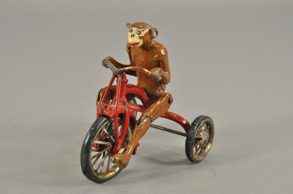 HUBLEY MONKEY RIDING TRICYCLE: An early novelty toy, cast iron, great depiction of monkey with articulated legs seemingly peddling bike, painted in brown, red bike, rubber tires, nickel poke wheels with clicker. 6 1/2" l.