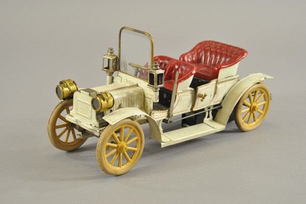 CARETTE FOUR-SEAT OPEN TOURER: Germany, c. 1912, hand painted tin, done in white body, embossed red seating, classic design with headlamps, side lanterns and glass windshield, rubber tires on spoke wheels, clockwork driven. 12 1/2"