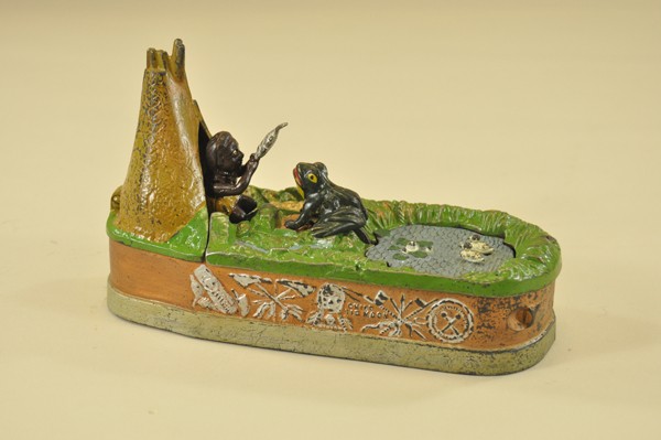 CHIEF BIG MOON MECHANICAL BANK: J & E Stevens Co., designed by Charles A. Bailey, patented 8/8/1899, tan base. Place the coin in slot in front of pond, press the lever, and as the coin disappears the frog springs from the water afte