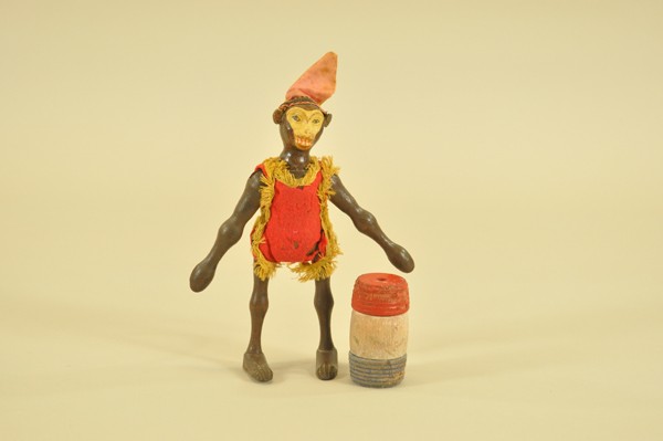 SCHOENHUT MONKEY AND BARREL: Hand painted composition head with leather ears, light & dark face variation. Red felt suit with yellow fringe, wears red & yellow satin hat, includes red, white & blue barrel. Monkey 8" h., barrels 3
