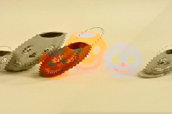 THREE HALLOWEEN JACK-O-LANTERNS: Unusual black example has menacing fangs, while both orange pieces have cheerful grins; all with paper backed faces, interior candle clips and wire handles, smallest has decorative crepe paper accordi