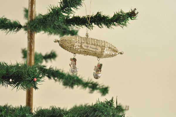 SEBNITZ GRAF ZEPPELIN WITH CHILDREN IN BASKETS: Wire covered pierced metal over crepe paper frame, two German scrap children in baskets hanging from the airship marked, "Graf Zeppelin". 5" t.