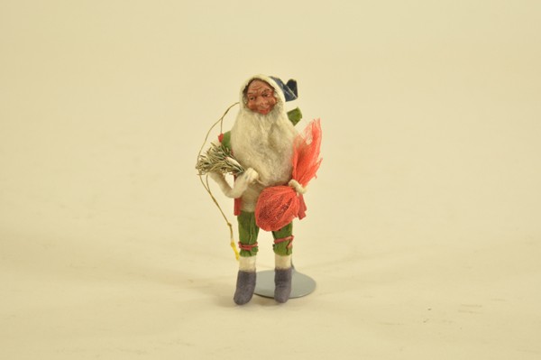 SPUN COTTON & CREPE PAPER ELF FIGURE: This early German Christmas tree ornament has a composition elf-like face, carrying a switch and a bag of coal, wearing a long blue cap and a red & green back pack, he must be looking for bad children