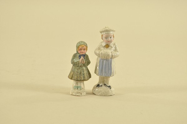 TWO EARLY GERMAN CANDY CONTAINERS: Composition, charming young girl figures, larger in white outfit and muff, covered in mica, smaller with hands in praying position and speckled green outfit, both open at hips. 3-3/4" - 5" t.
