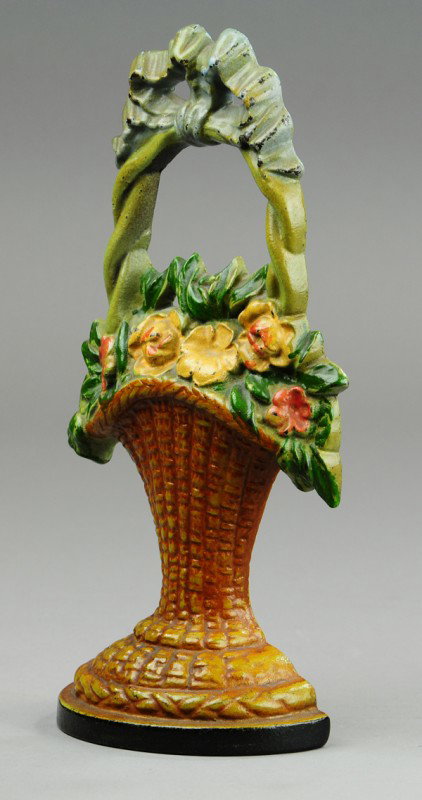 FLOWER BASKET WITH LARGE BOW DOORSTOP: Cast iron, wicker basket casting, red and yellow floral arrangement, large blue bow on top of handle. 11 1/2" h.