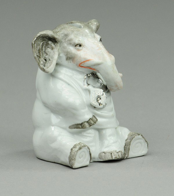 SEATED ELEPHANT PORCELAIN STILL BANK: Germany, c. 1920, whimsical pose, colored in light and dark greys, silver lock on chest, coin slot in head. 3 3/8" h.