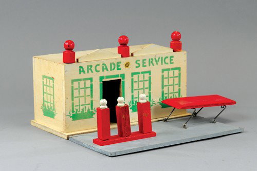 ARCADE WOOD SERVICE STATION: Painted in white with green stenciled window and doorways, original Arcade decal on front, piece comes with grey driveway base, fuel pump island and car ramp, opening garage bay door. 12" wide.
