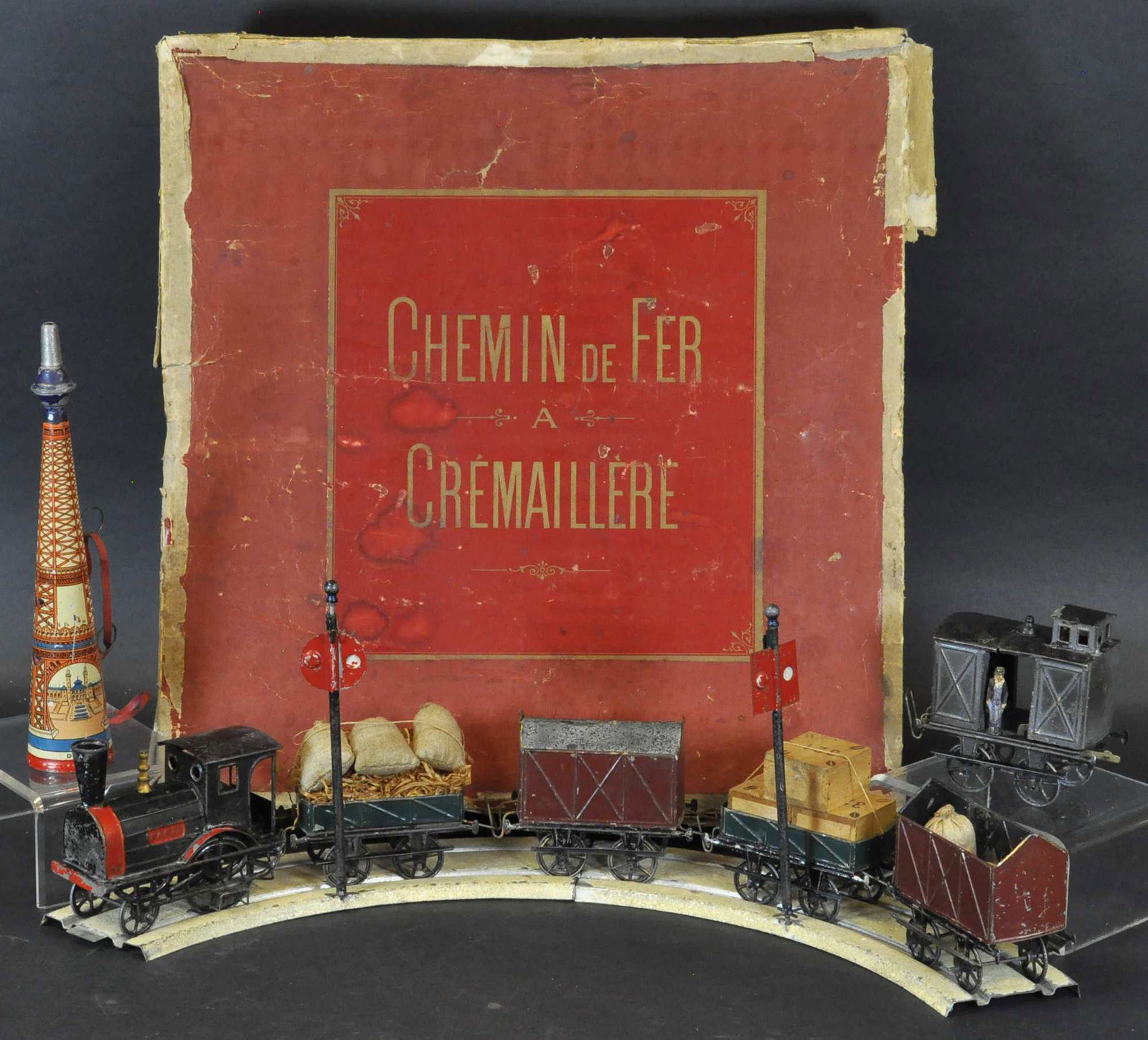 BOXED TANTET & MANON CATASTROPHIE TRAIN: 303. BOXED TANTET & MANON CATASTROPHIE TRAIN | France, c. 1890, w/ box, fly wheel driven. | Loco 4.5" l. | Box worn with some tears, train (Exc. Cond.) for age. | $2,000 - $3,000