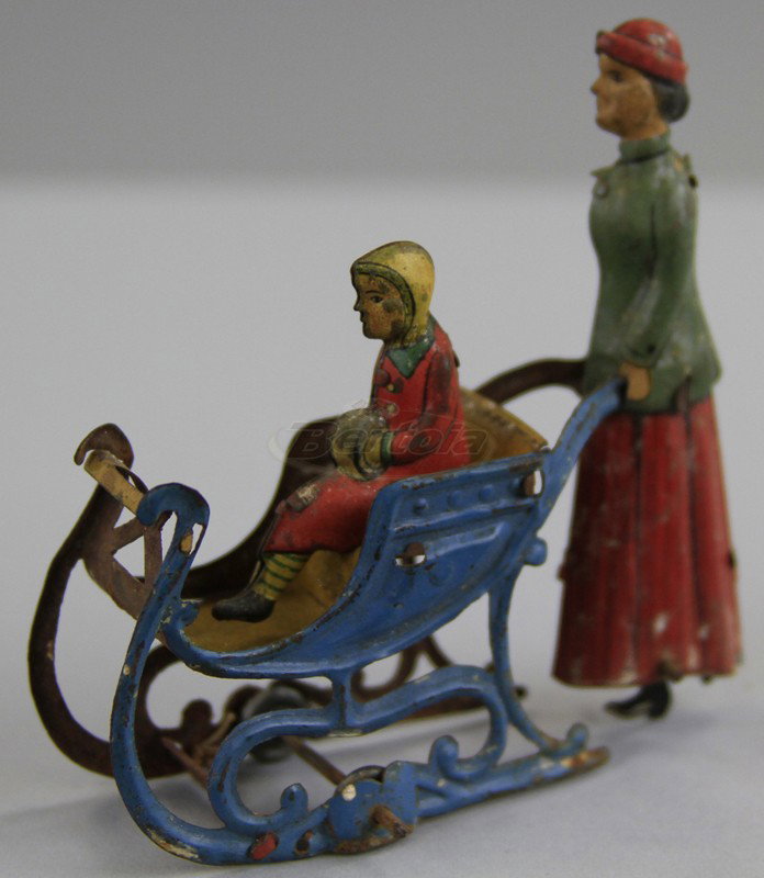 WOMAN PUSHING CHILD IN SLEIGH PRAM PENNY TOY: Meier, Germany, lithography depicts woman pushing child in ornate pram, feet die cut as wheel which revolves. 2 3/4" l.