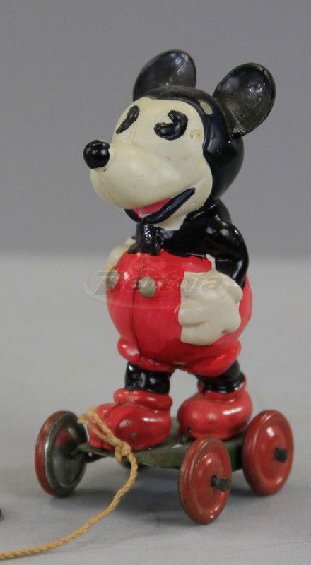 MICKEY MOUSE ON TIN BASE: Japan, celluloid figure of Mickey Mouse standing on small wheeled tin base, original pull string with ring holder, label on body. 3 1/4" h.