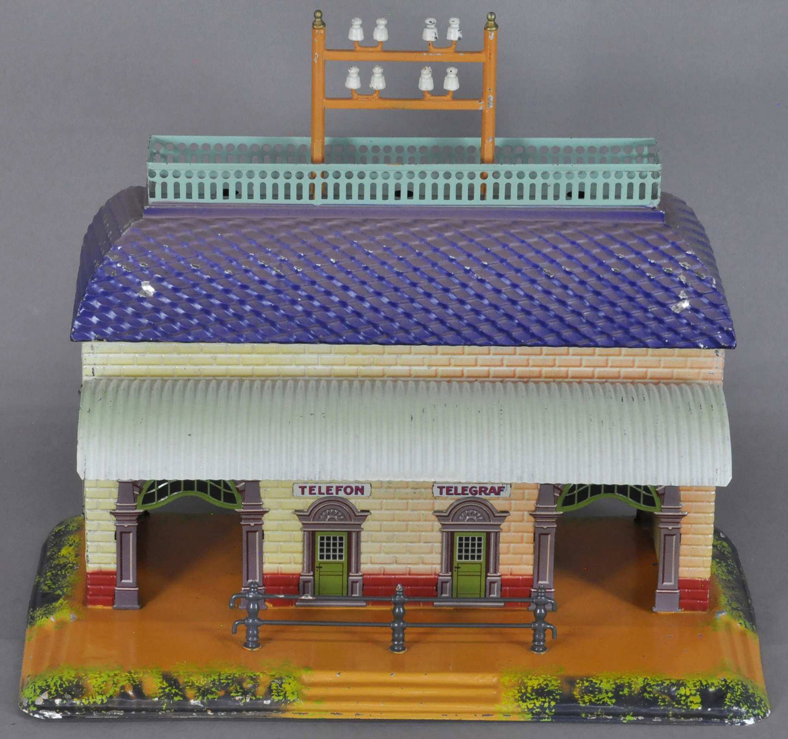 EARLY BING STATION W/ CANOPY: 105. EARLY BING STATION W/ CANOPY | Germany, c. 1910, lithographed tin, very colorful overall, features two doorways, embossed brick pattern building, railed portion on base, telegraph poles at emboss