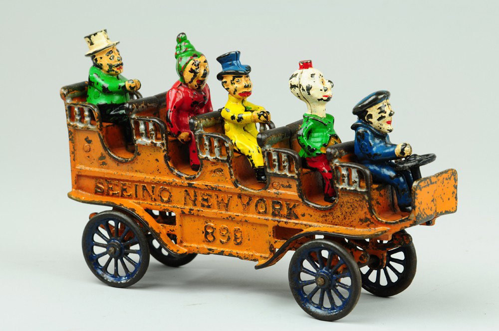 KENTON SEEING NEW YORK BUS: C. 1910, a scarce and desirable cast iron toy, painted in orange body, features seated comic character figures. 10 1/4" l.