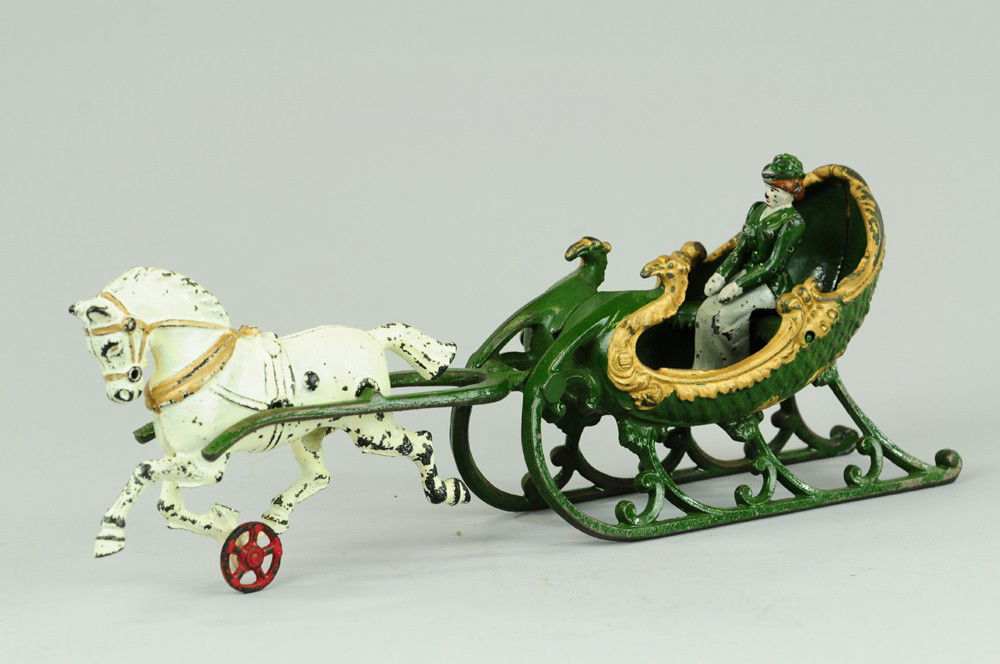 ONE HORSE OPEN SLEIGH: Hubley, dark green and gold sleigh pulled by white horse trimmed in gold, front of sleigh swirls up in attractive swan design, embossed seating with woman driver. 15 1/4" l.