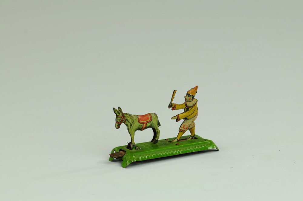 CLOWN CHASING DONKEY PENNY TOY: Meier, Germany, lithographed tin, humorous depiction of clown w/stick chasing donkey. 3 3/4" l.