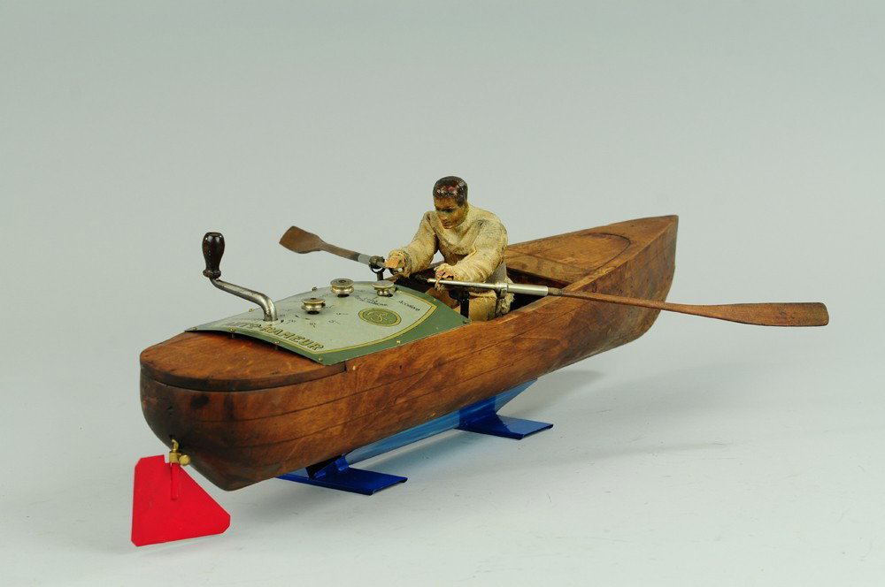 MECHANICAL ROWER IN WOOD BOAT: France, Auto-Rameur, heavily carved hull, tin plate on deck features control knobs and clockwork lever, seated rower done in composition head, cloth body, realistic rowing action, some fraying to clot
