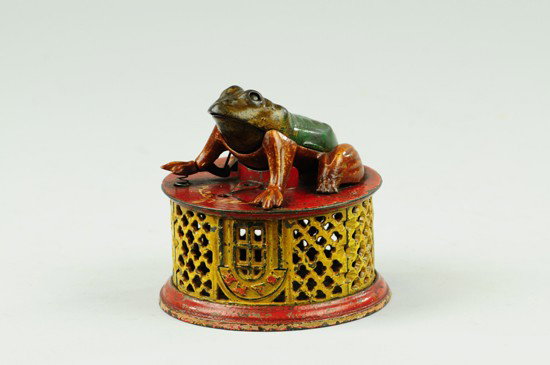 FROG ON ROUND BASE MECHANICAL BANK: Red and yellow base, J & E Stevens Co., circa 1870's, red lattice base. By pressing one foot, the frog's mouth opens to receive a coin, which is swallowed upon releasing the foot from pressure; the ey
