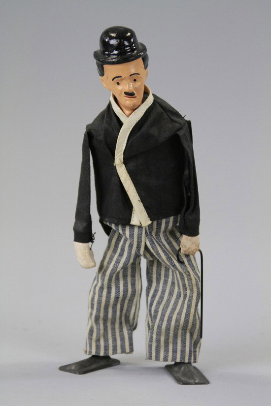 CHARLIE CHAPLIN WALKING FIGURE: Composition head, cloth outfit, lead shoes, attributed to French made, holds hat and cane in hand, key wind operated. 7 1/2" h.