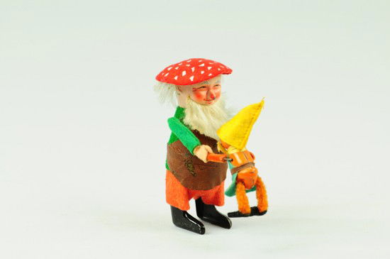 GNOME WITH CHILD: Schuco, Germany, clockwork driven, wears green felt jacket, red shorts, brown leather apron, red mushroom cap hat, grey and white hair and beard, painted face with long nose, holds small child in danc