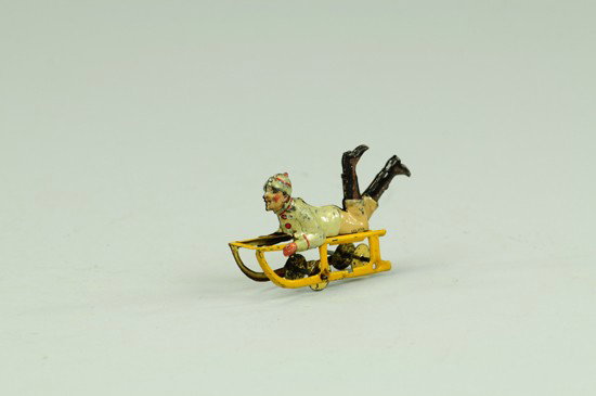 BOY ON SLED PENNY TOY: Meier, Germany, lithographed tin, depicts elated boy with legs in air on trestle, sled in yellow. 3 1/2" l.