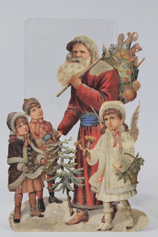LARGE SANTA DIE CUT WITH CHILDREN: Santa die cut store display features Santa with pack of toys holding a feather tree, two children look up at Santa admiringly, Angel rings bells, decorated with crushed glass throughout. 20" h.
