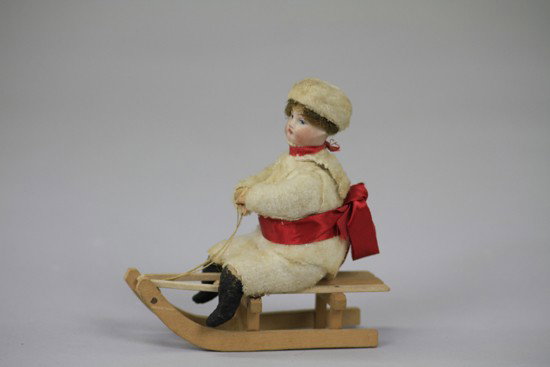 BISQUE HEAD CHILD ON SLED: Germany, Heubach spun cotton body with hair under hat, on wooden sled, realistic example with finely detailed expression. 4 1/4" h.