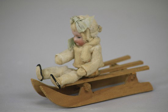 BISQUE HEAD BABY ON WOOD SLED CANDY CONTAINER: Heubach, Germany, bisque head baby with real hair, spun cotton body opens at the waist for candy retrieval. 5 1/2" l.