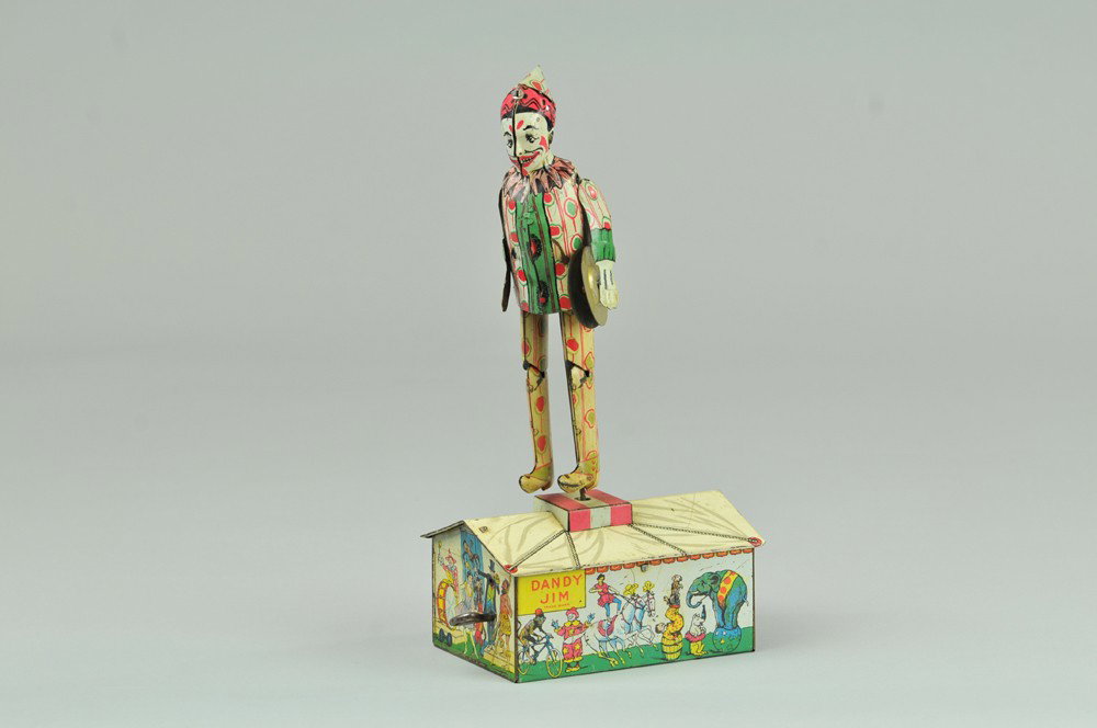 DANDY JIM JIGGER: Unique Art., copr. 1922, lithographed tin, depicts colorful clown onstage base, clockwork driven. 10 1/4" h. NOTE: Hand tab is broken.