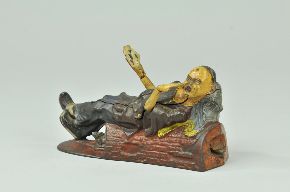 RECLINING CHINAMAN MECHANICAL BANK: J & E Stevens Co., designed by James H. Bowen, circa 1885. Place the coin in the opening. Press the lever, and the Chinaman will show his hand (four aces) and salute the depositor. As the coin falls i
