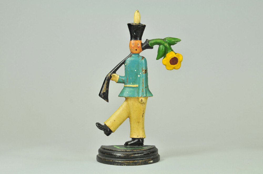 SOLDIER WITH FLOWER IN GUN DOORSTOP: BOOK EXAMPLE, "10001" on back, great whimsical cast iron figure of soldier in marching stance with bold flower drooping out of gun barrel, very rare. 12 7/8" x 7 1/8". (Pristine Cond.) 12 7/8" x 7 1/8