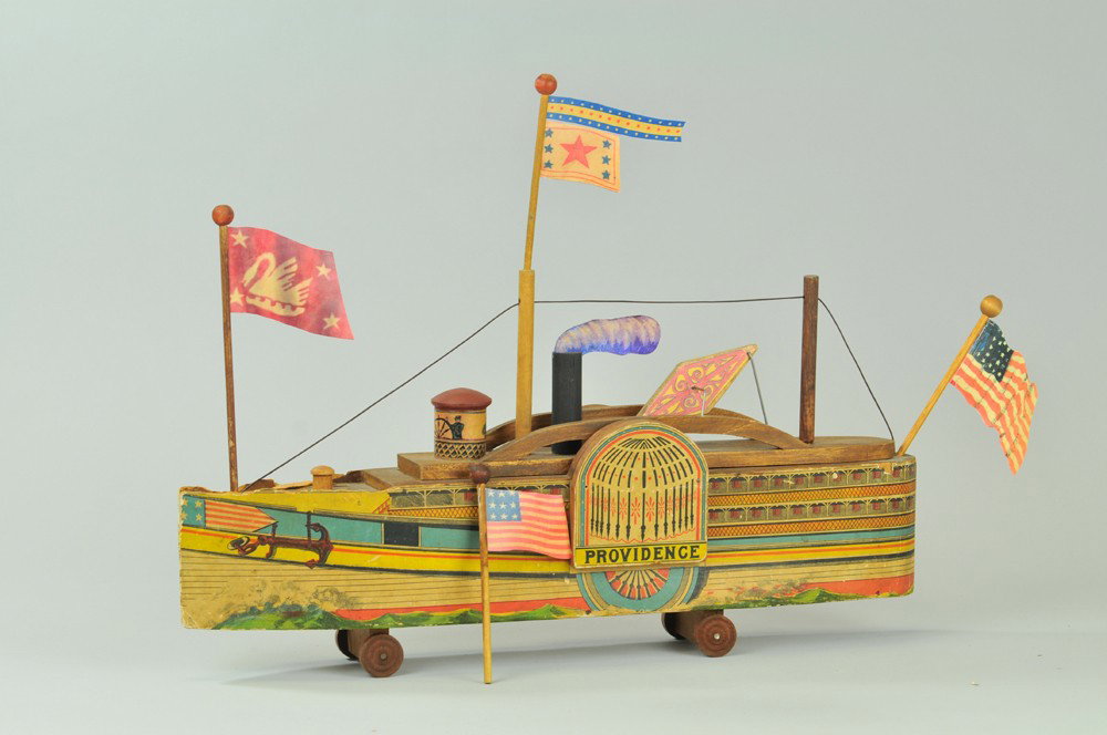 BLISS "PROVIDENCE" PADDLEWHEEL BOAT: Another of the early Bliss boats, litho paper on wood portrays multi-level vessel with large anchor at bow, bright colors throughout, one wheel chipped, small hole at hull, smoke billow replaced. 20" 