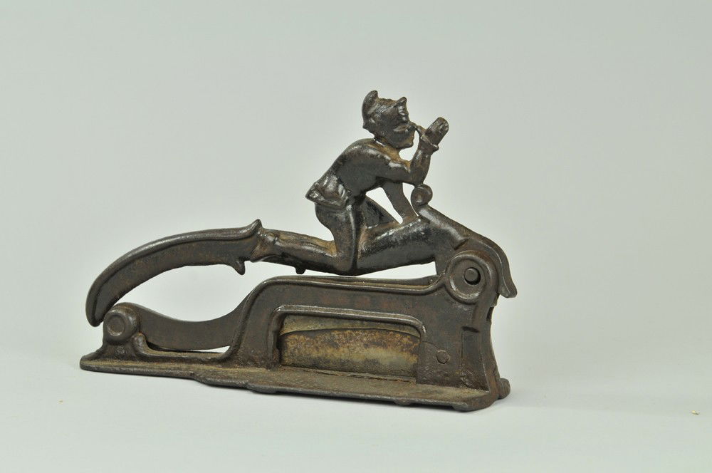 ELF FIGURAL PLUG TOBACCO CUTTER: Mfg. by Brighton, cast iron countertop plug cutter with elf figure on handle, well cast, a classic image. 11" l. Paint worn. (VG Cond) 11" l.