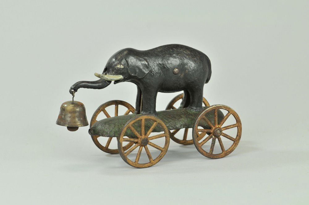 ELEPHANT BELL TOY: N.N. Hill, c. 1905, cast iron elephant cast base with articulated trunk, holds bell, yellow spoke wheels, older bell but a replacement. 6 3/4" l. (VG Cond) 6 3/4" l.